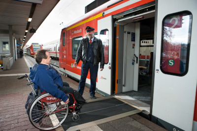 Ein DB-Mitarbeiter hilft einem Rollstuhlfahrer an der Einstiegsrame